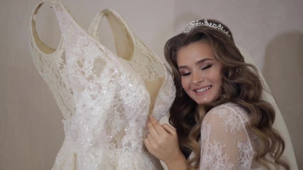 Όμορφη και όμορφη νύφη σε νυχτικό και πέπλο στέκεται κοντά στο νυφικό — Αρχείο Βίντεο