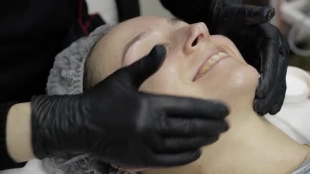 Cosmetoloog brengt hydraterende crème op vrouw gezicht in schoonheidssalon — Stockvideo