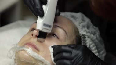 Güzellik salonunda kozmetik uzmanı kadın yüzüne ultrasonik yüz temizliği yapıyor.