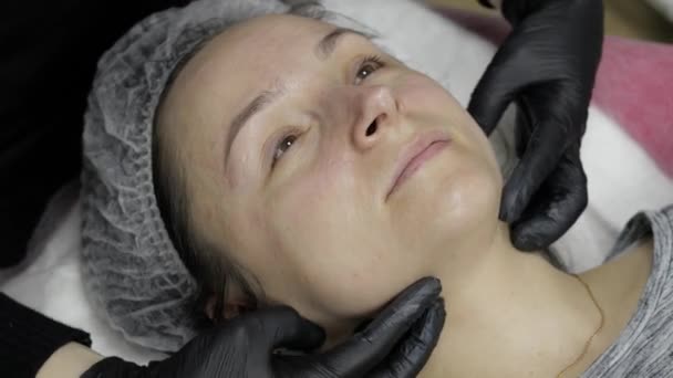 Косметолог наносит увлажняющий крем на лицо женщины в салоне красоты — стоковое видео