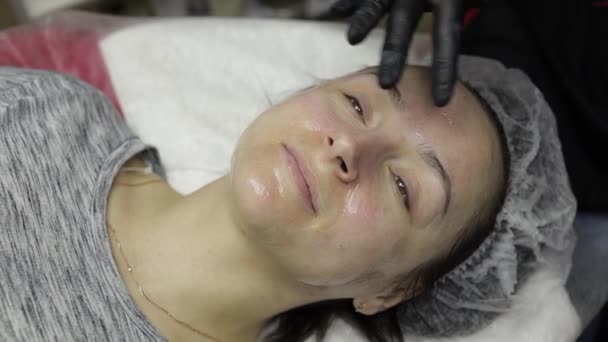Cosmetólogo aplica loción peladora en la cara de la mujer en salón de belleza clínica — Vídeo de stock