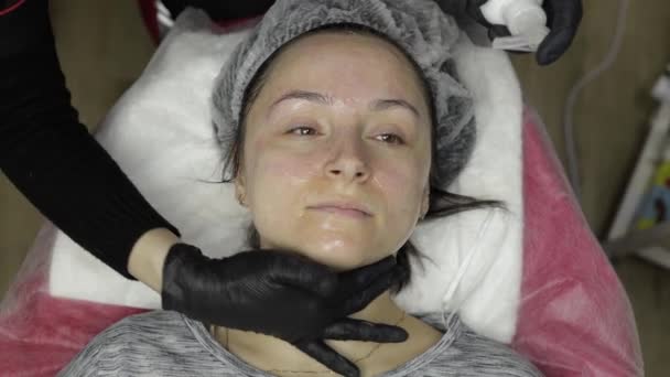 Kosmetolog stosuje peeling balsam na twarzy kobiety w salonie kosmetycznym — Wideo stockowe