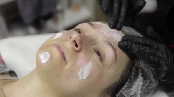 Cosmetoloog brengt hydraterende crème op vrouw gezicht in schoonheidssalon — Stockvideo