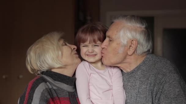 Grandfather and grandmother kissing on cheeks their kid granddaughter at home — Stock Video