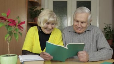 Mutlu yaşlı büyükanne ve büyükbaba çift evde masada oturup kitap okumanın keyfini çıkarıyorlar.