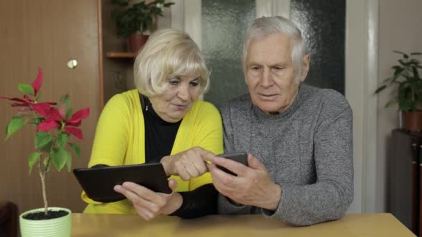 Vrij volwassen senior paar grootouders genieten van online winkelen op telefoon, tablet — Stockvideo