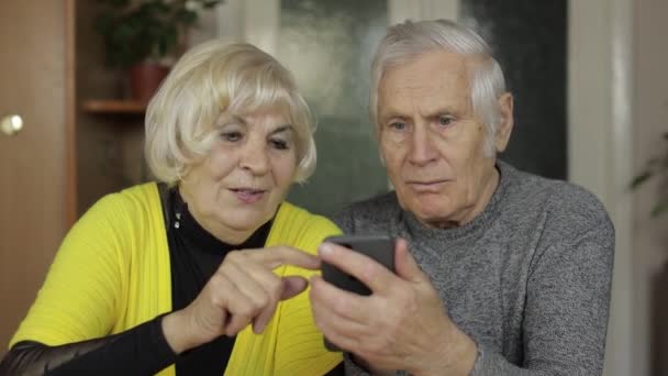 Pretty mature senior couple grandparents enjoy online shopping on phone at home — Stock Video