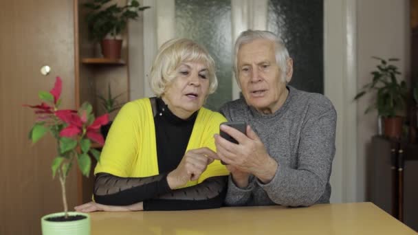 Pretty mature senior couple grandparents enjoy online shopping on phone at home — Stock Video