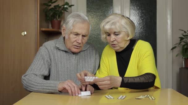 Старые бабушка и дедушка смотрят на таблетки, таблетки в волдырях на столе дома — стоковое видео