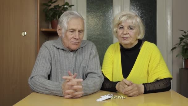 Oude grootouders kijken naar pillen, tabletten in een blisterverpakking op tafel thuis — Stockvideo