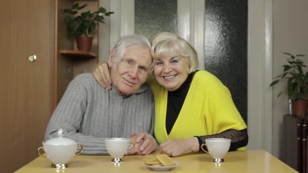 Happy old grandparents couple sit on table at home enjoy drinking tea together — Stock Video