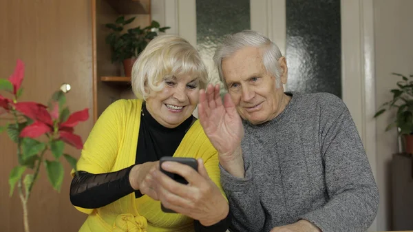 Bastante madura pareja de abuelos haciendo videollamada con teléfono en casa — Foto de Stock