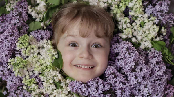 Menina bonito criança olhando de ramo buquê de flores lilás em torno de seu rosto — Fotografia de Stock