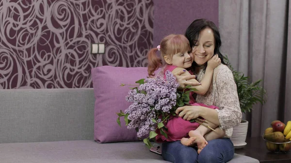 Kleine dochter en moeder zitten op sofe met boeket van lila paarse bloemen — Stockfoto