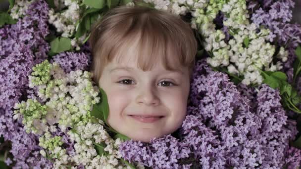 Söt flicka barn tittar från ett gäng bukett lila blommor runt ansiktet — Stockvideo