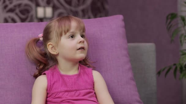 Little child sitting on couch while watching TV. Kid girl watch television — Stock Video