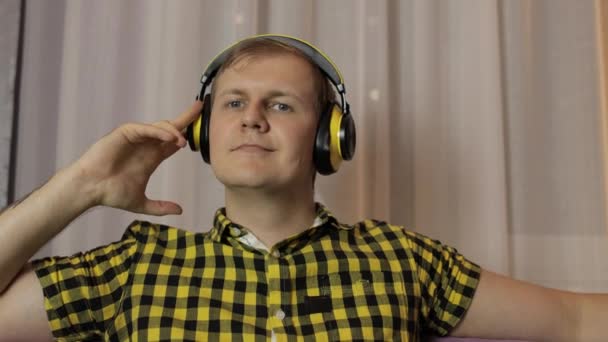 Mężczyzna siedzący na kanapie słucha muzyki z bezprzewodowych słuchawek i tańców — Wideo stockowe