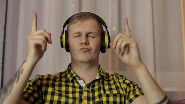 Чоловік сидить на дивані слухає музику з бездротових навушників і танців — стокове відео