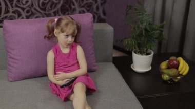 Küçük çocuk televizyon izlerken kanepede oturuyor. Küçük kız televizyon izliyor.