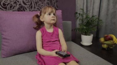 Küçük çocuk televizyon izlerken kanepede oturuyor. Küçük kız televizyon izliyor.