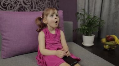 Küçük çocuk televizyon izlerken kanepede oturuyor. Küçük kız televizyon izliyor.