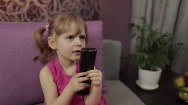 Küçük çocuk televizyon izlerken oturuyor. Mutlu kız çocuğu komik bir müzik filmi izliyor.