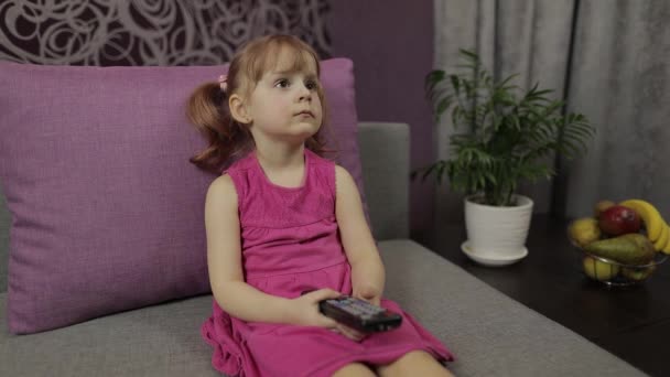 Pequeño niño sentado en el sofá mientras ve la televisión. Niña ver televisión — Vídeos de Stock