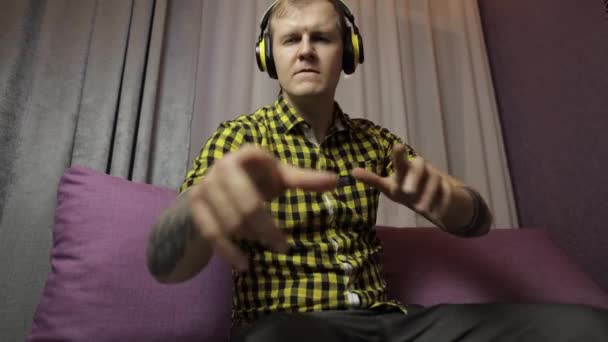 Muž sedící na pohovce poslouchá hudbu z bezdrátových sluchátek a tanců — Stock video