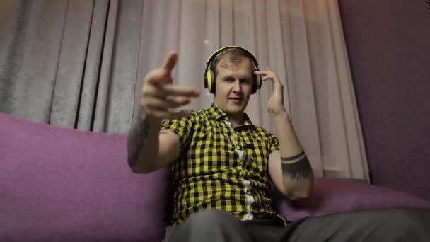 Férfi ül a kanapén hallgat zenét vezeték nélküli fejhallgató és táncok — Stock videók