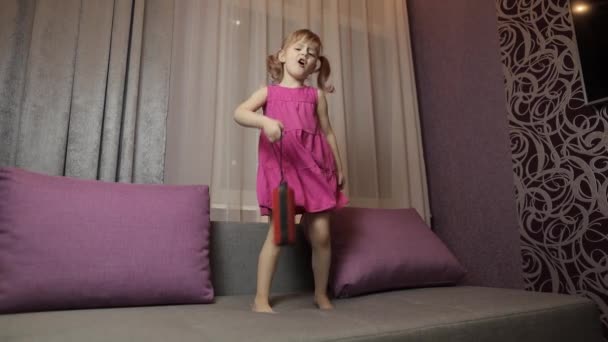 Gyermek lány vezeték nélküli hangszóróval élvezi a zenét. Otthon a kanapén táncolok. — Stock videók