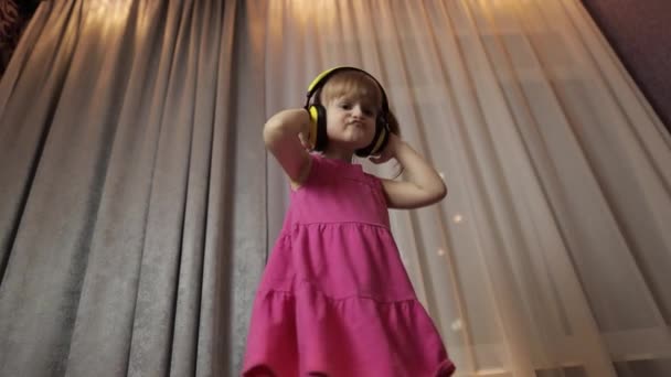 ワイヤレスヘッドフォンで小さな子供の女の子は音楽を聴くを楽しんでいます。自宅で踊る — ストック動画