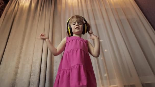 Egy kislány vezeték nélküli fülhallgatóban zenét hallgat. Otthon táncolok. — Stock videók
