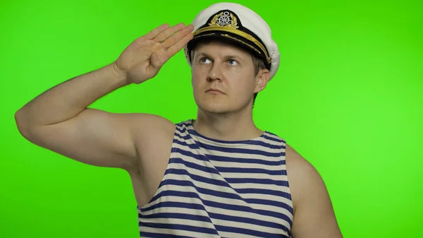 Young sailor man salutes with hand, looking up. Seaman guy in sailors vests