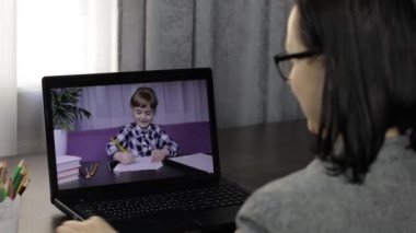 Bayan öğretmen küçük bir öğrenciyle bilgisayardan video görüşmesi yapıyor. Uzaklık eğitimi