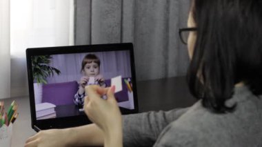 Bayan öğretmen küçük bir öğrenciyle bilgisayardan video görüşmesi yapıyor. Uzaklık eğitimi