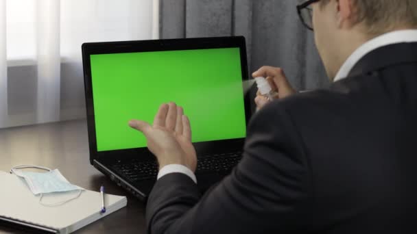 L'uomo prende bottiglia igienizzante e utilizzare vicino computer portatile con schermo verde. Lavoro a distanza — Video Stock