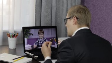 Erkek öğretmen laptopta küçük bir öğrenciyle video görüşmesi yapıyor. Uzaklık eğitimi