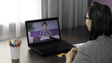 Bayan öğretmen küçük bir öğrenciyle bilgisayardan video görüşmesi yapıyor. Uzaklık eğitimi