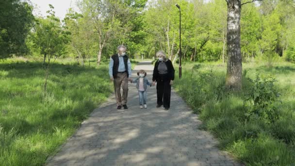 Viejos abuelos con nieta en máscaras médicas caminan en el parque. Coronavirus — Vídeos de Stock