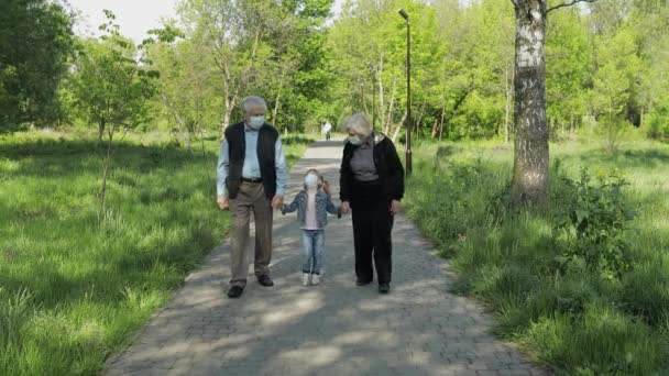 Old grandparents with granddaughter in medical masks walk in park. Coronavirus — Stock Video