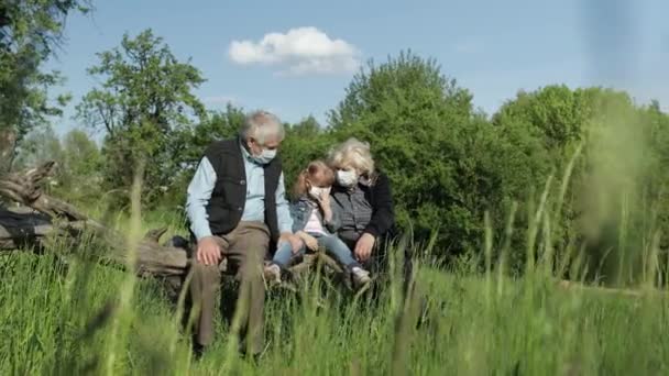 Grootouders met kleindochter met medische maskers in het park. Quarantaine van het coronavirus — Stockvideo