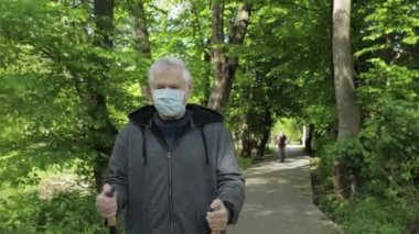 Karantina sırasında parkta yürüyen maskeli kıdemli yaşlı adam.