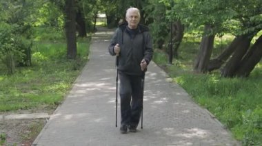 Aktif kıdemli yaşlı adam parkta kayak direkleri ile İskandinav yürüyüşü eğitimi alıyor.
