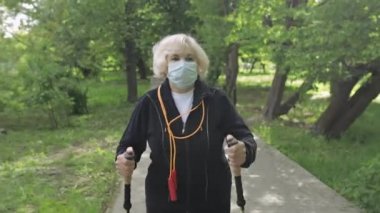 Karantinada parkta yürüyen, maske eğitimi alan kıdemli yaşlı kadın.