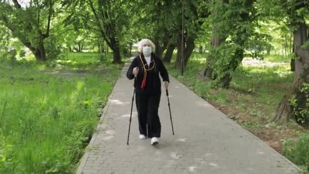 Actieve oudere vrouw in maskertraining Nordic walking in park in quarantaine — Stockvideo
