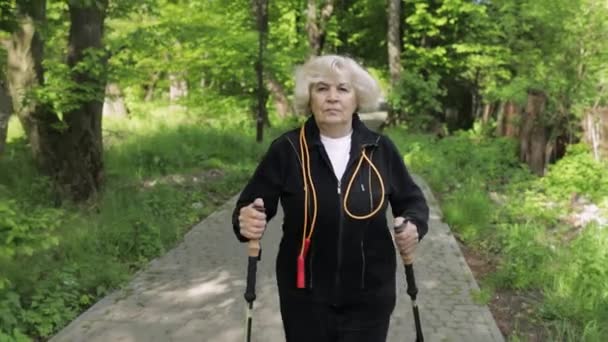 Actieve oudere vrouw traint Nordic walking met ski trekking stokken in het park — Stockvideo