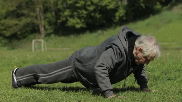 Vieil homme âgé actif faire des exercices physiques push-ups dans le terrain de sport — Video