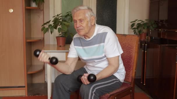Yaşlı, beyaz bir adam ağırlık kaldırıyor. Evde halter egzersizi yapıyor. — Stok video