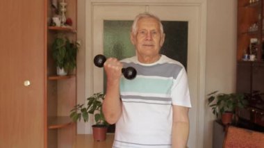 Yaşlı, beyaz bir adam ağırlık kaldırıyor. Evde halter egzersizi yapıyor.