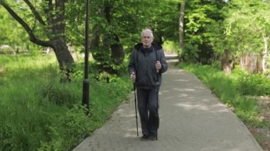 Aktif kıdemli yaşlı adam parkta kayak direkleri ile İskandinav yürüyüşü eğitimi alıyor.
